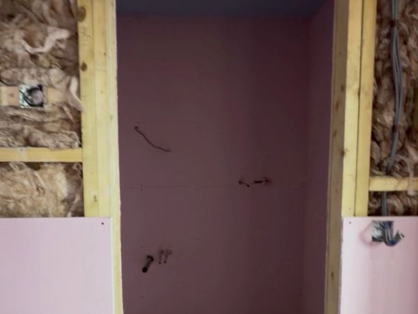 Partially constructed wall with insulation and pink drywall panels installed.