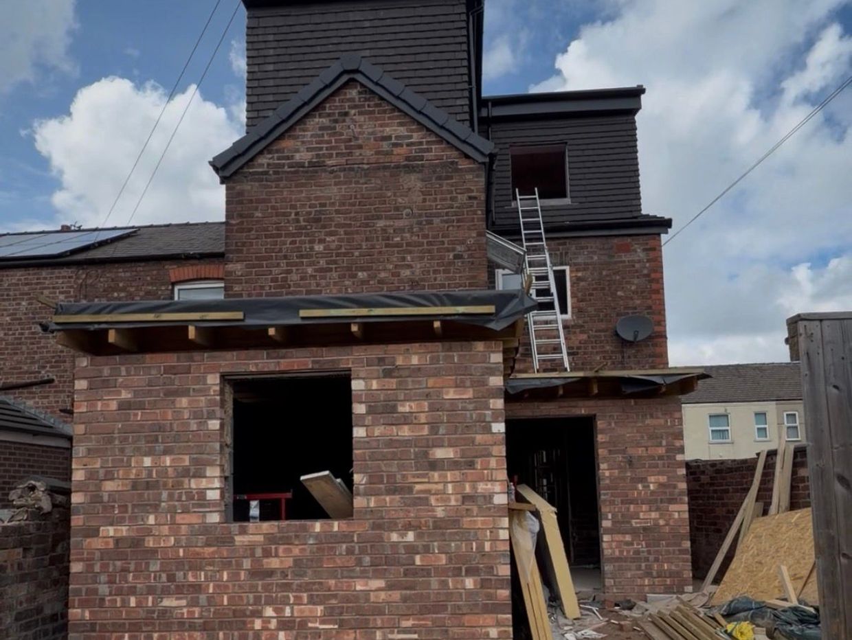 Brick house under construction with ladders and building materials.