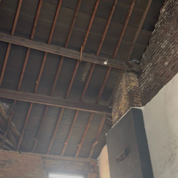 Exposed wooden ceiling beams in a rustic brick room with a window.