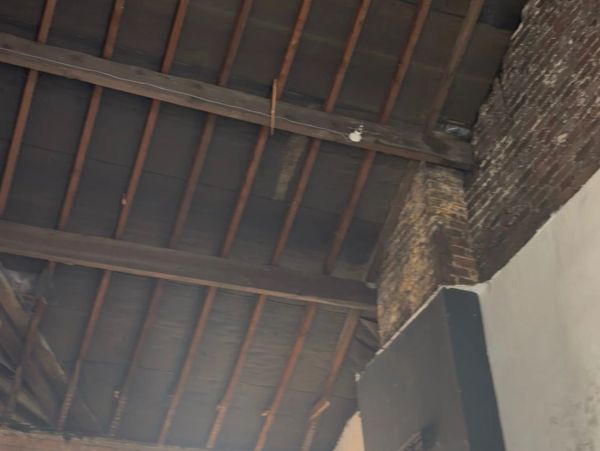 View of an old wooden ceiling with beams and brick walls.