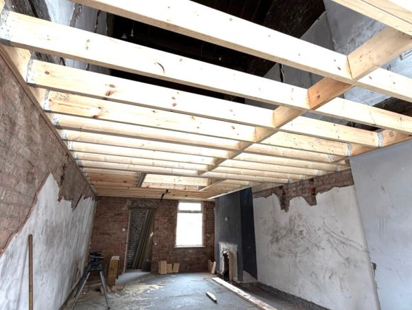 Room under renovation with exposed wooden ceiling beams and unfinished walls.