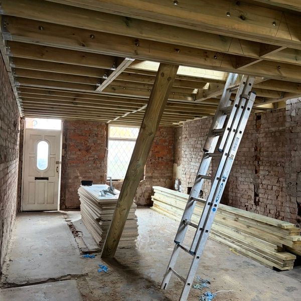 Interior view of a construction site with wooden beams and a ladder.