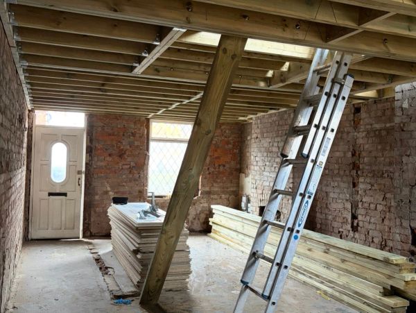 Interior view of a construction site with wooden beams and a ladder.