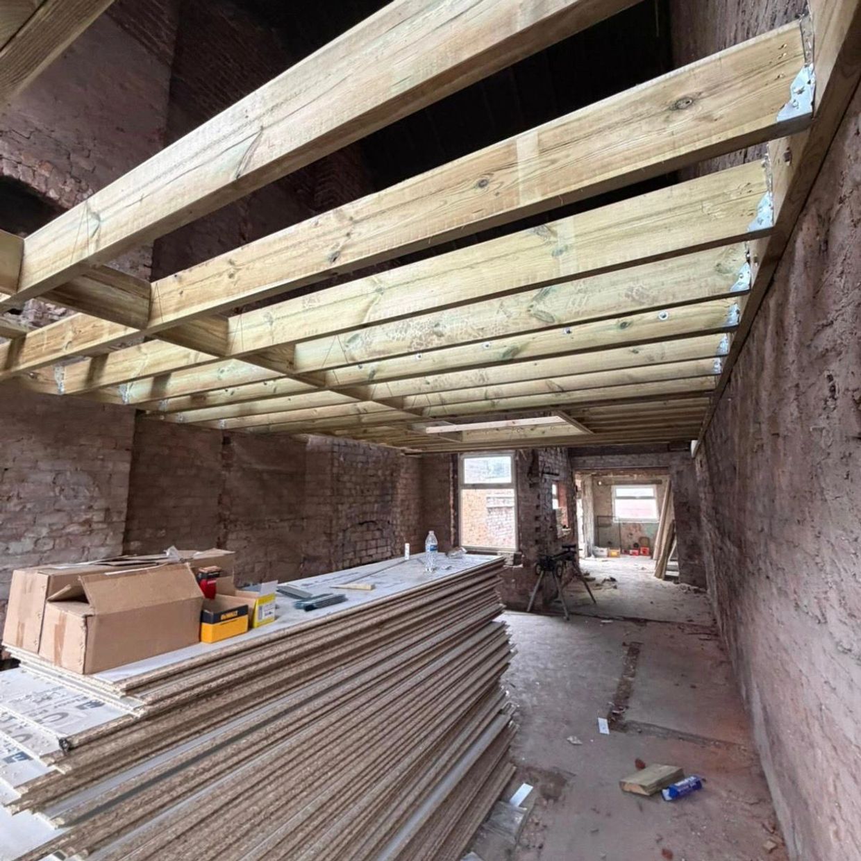 Interior of a building under construction with wooden beams and stacked drywall sheets.