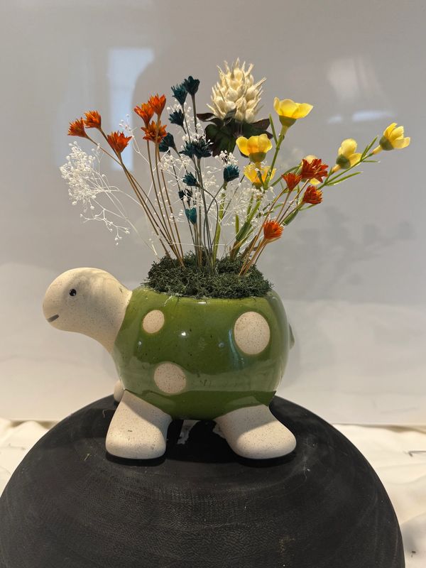 A turtle-shaped ceramic vase with colorful artificial flowers.