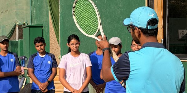 Coach instructs young tennis players during practice on a sunny day.