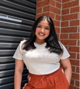 Smiling woman in white shirt and rust-colored pants.