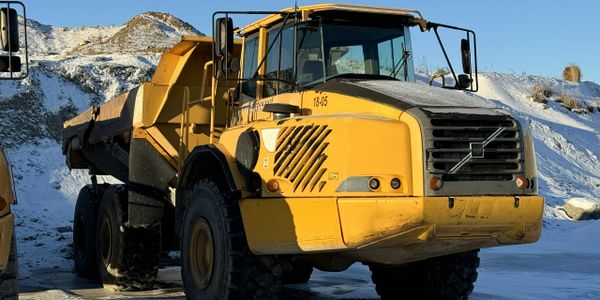 Yellow Volvo dump truck parked on snowy ground with a clear blue sky.