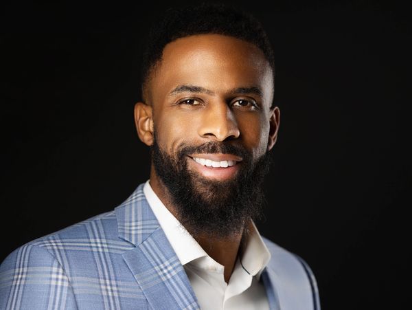 Smiling man in a blue plaid suit jacket with a black background.