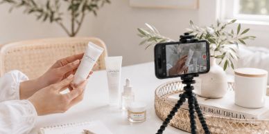 Person holding skincare product while filming with a smartphone on a tripod.