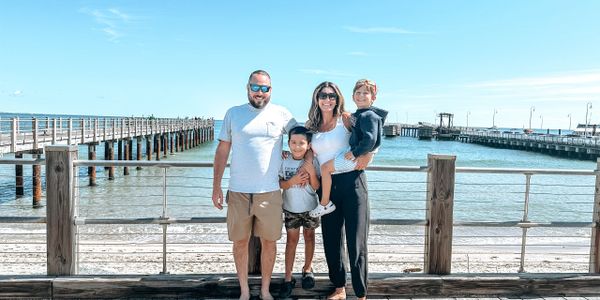 A happy family of four posing by the waterfront on a sunny day.