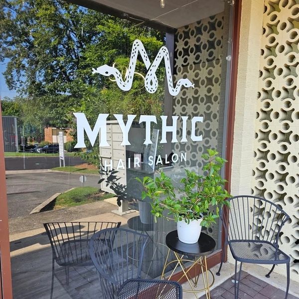 Entrance of Mythic Hair Salon with two black chairs and a small table with a plant.