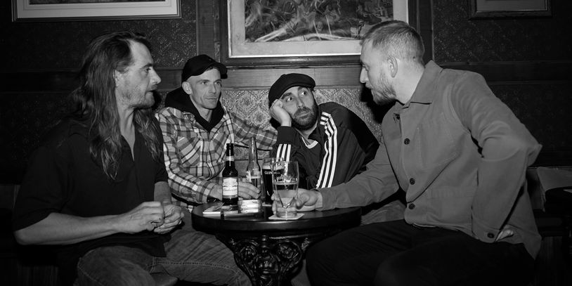 Four men sitting around a table in a pub, engaged in conversation with drinks.