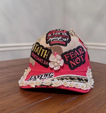 Decorated cap with faith-themed patches and floral accents on a wooden table.