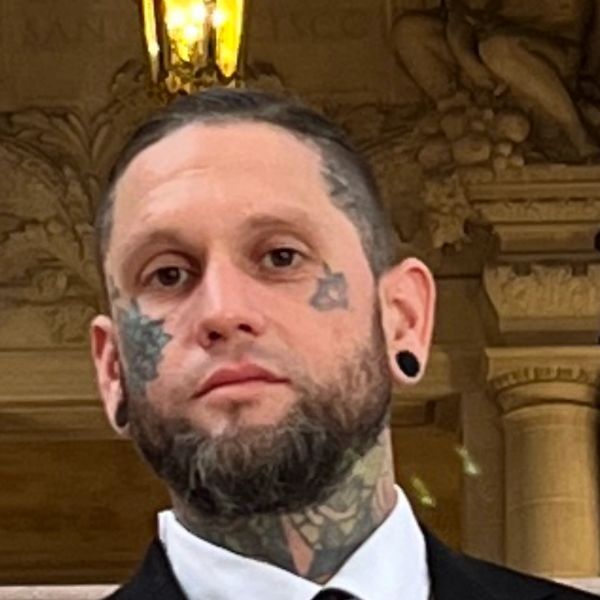 Man with facial and neck tattoos in formal wear.