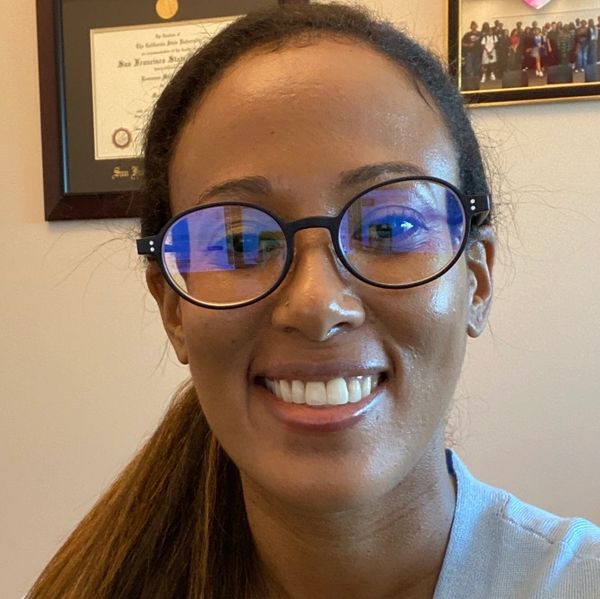 Smiling woman wearing glasses with certificates on the wall.