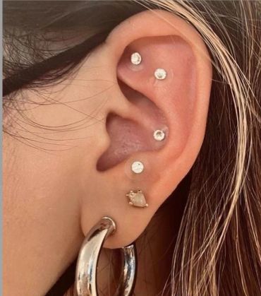 Ear with multiple diamond-style piercings and a large hoop earring.