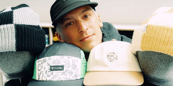 A man with hats balanced around his head, smiling gently.
