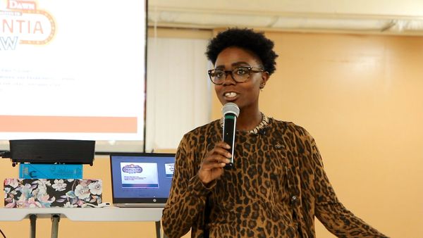 Speaker Arlieta Hall talks into a mic with a projector behind her