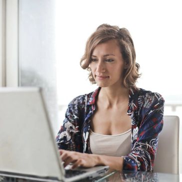 A woman working on a laptop at a glass table indoors.