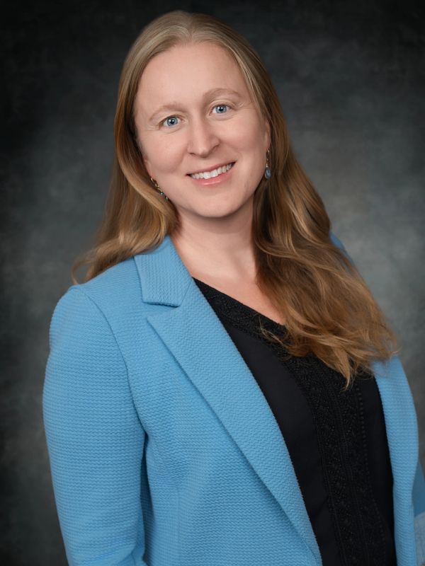 Woman smiling in a blue blazer against a dark background.