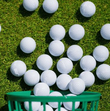 Several white golf balls on green grass near a basket.