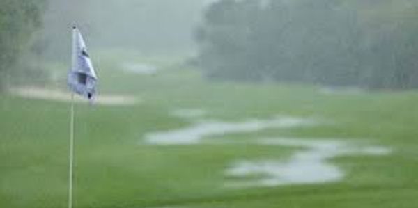 Golf course flagstick on a rainy day with puddles forming on the green.