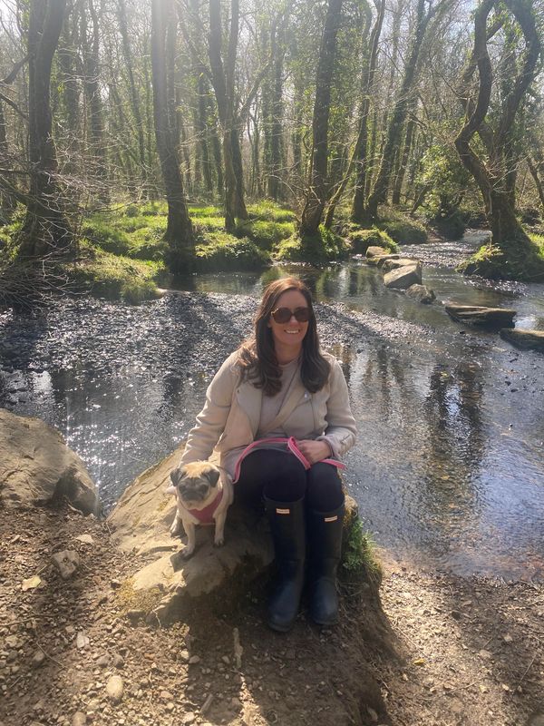 Woman sitting on a rock by a stream with her small dog on a sunny day.