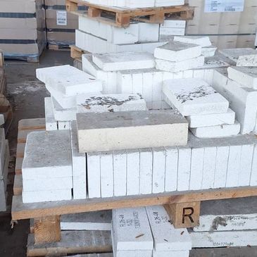Stacks of white bricks and blocks on wooden pallets in a warehouse.