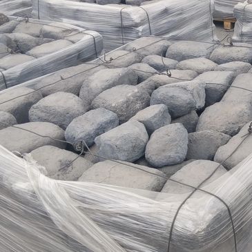 Pallets of large rocks wrapped in plastic and secured with wire outdoors.