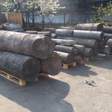 Stacks of large cylindrical metal ingots on pallets outdoors.