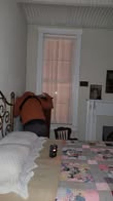 Person bending over near a bed in a dimly lit room.