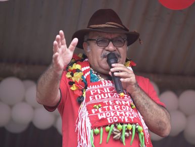 Man in a hat speaking passionately with a microphone and colorful accessories.