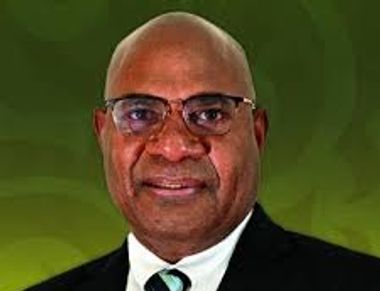 Portrait of a bald man wearing glasses and a suit against a green background.