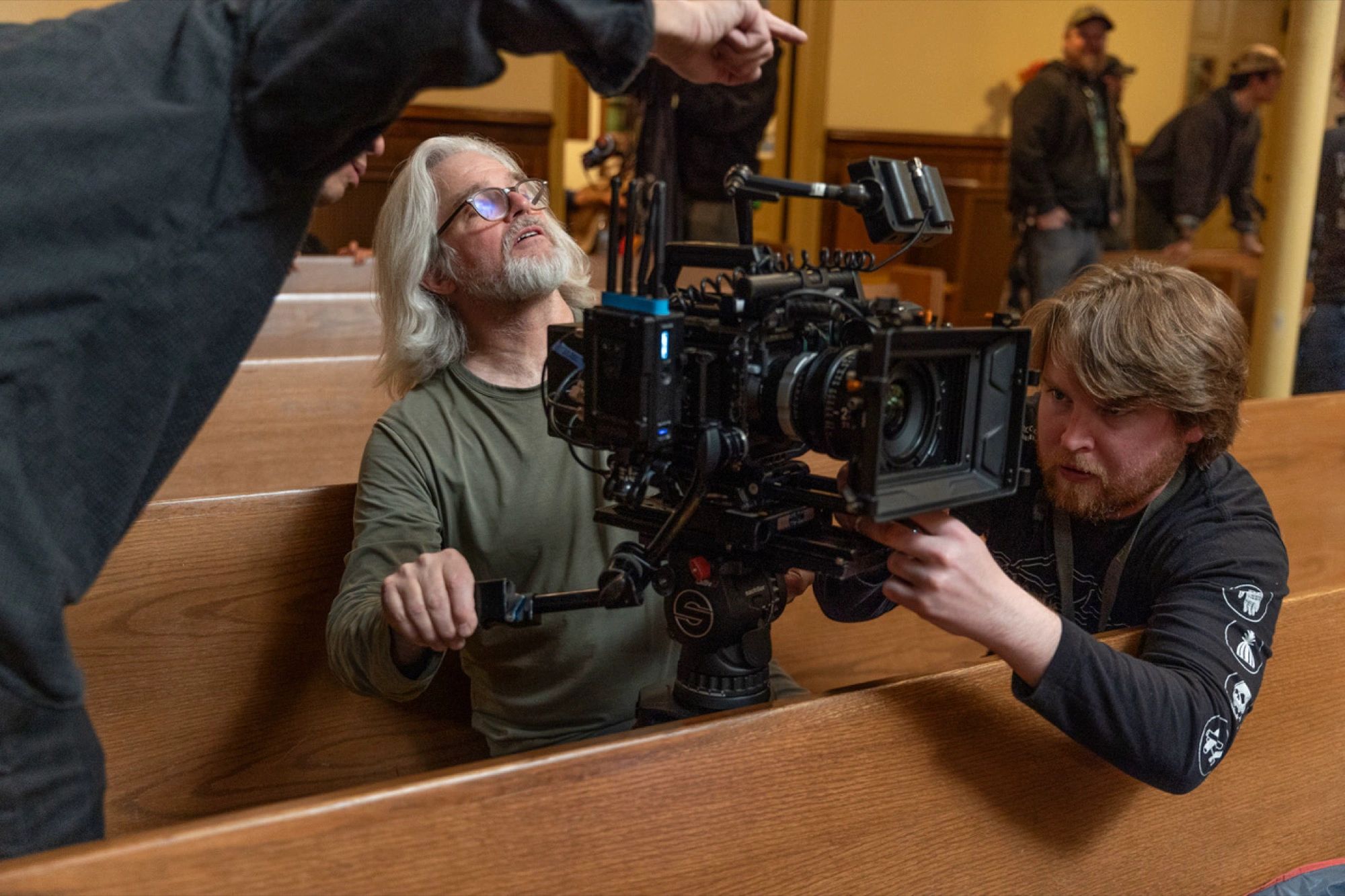 Crew members operate a professional camera inside a wooden pew area.