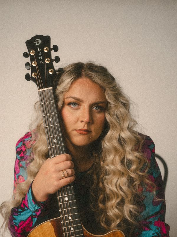 Woman holding a Luna guitar, looking thoughtfully.