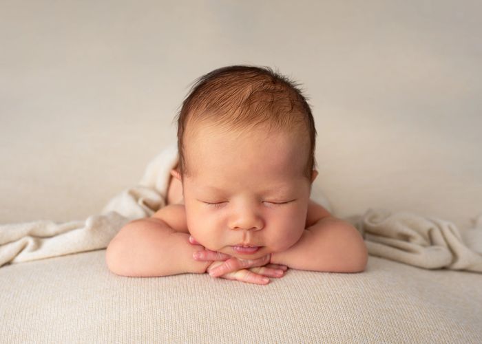 Sleeping newborn baby resting with folded arms on a soft beige blanket.
