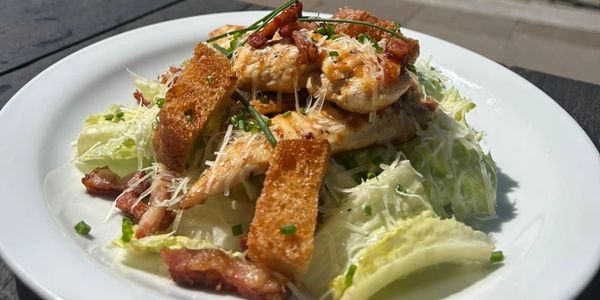 Grilled chicken salad with crispy bacon, croutons, and shredded cheese.