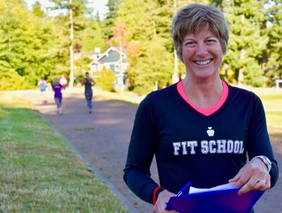 Smiling woman in a Fit School shirt holding a clipboard outdoors.