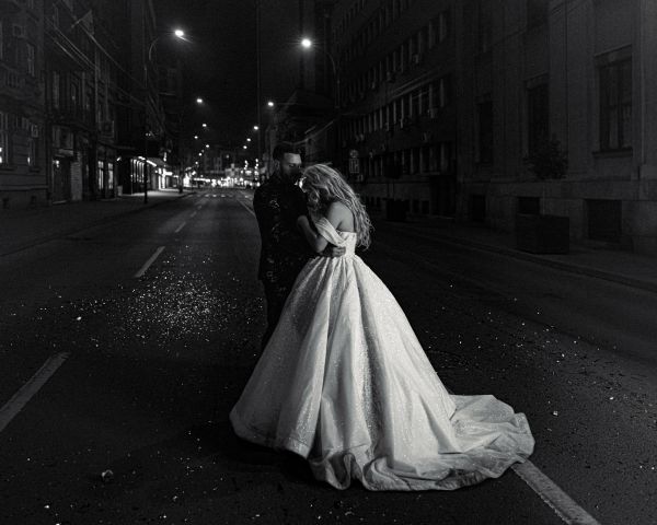 Couple embraces on an empty city street at night, bride in flowing gown.