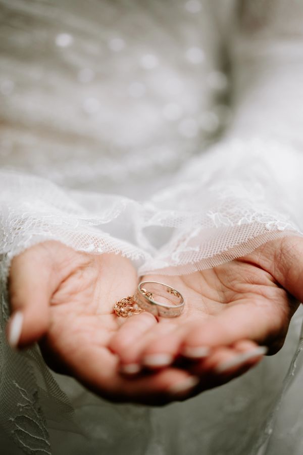 Hands holding two wedding rings against a lace fabric background.