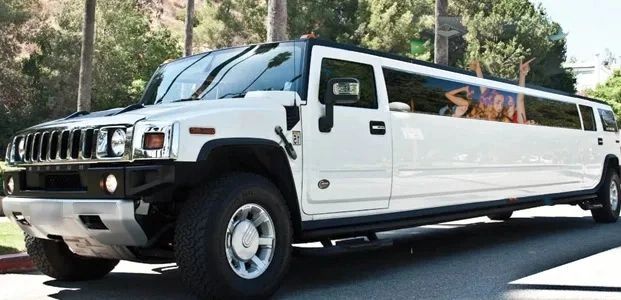 White stretch Hummer limousine parked outdoors with people visible inside.