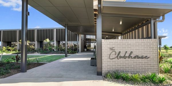 Modern clubhouse entrance with a covered walkway and landscaped greenery.