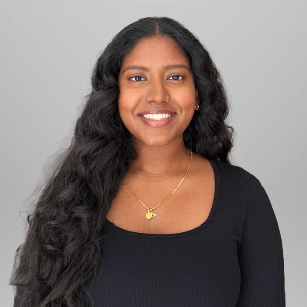 Smiling woman with long curly hair wearing a black top and gold necklace.