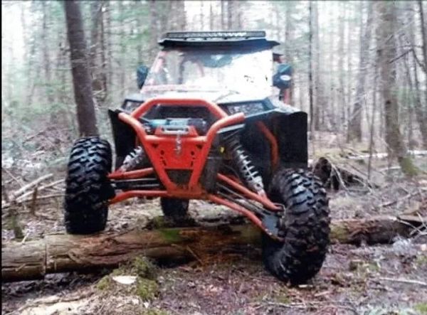 Red off-road vehicle with rugged tires crossing a log in a forest.