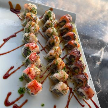 Three rows of assorted sushi rolls beautifully drizzled with sauces on a white plate.