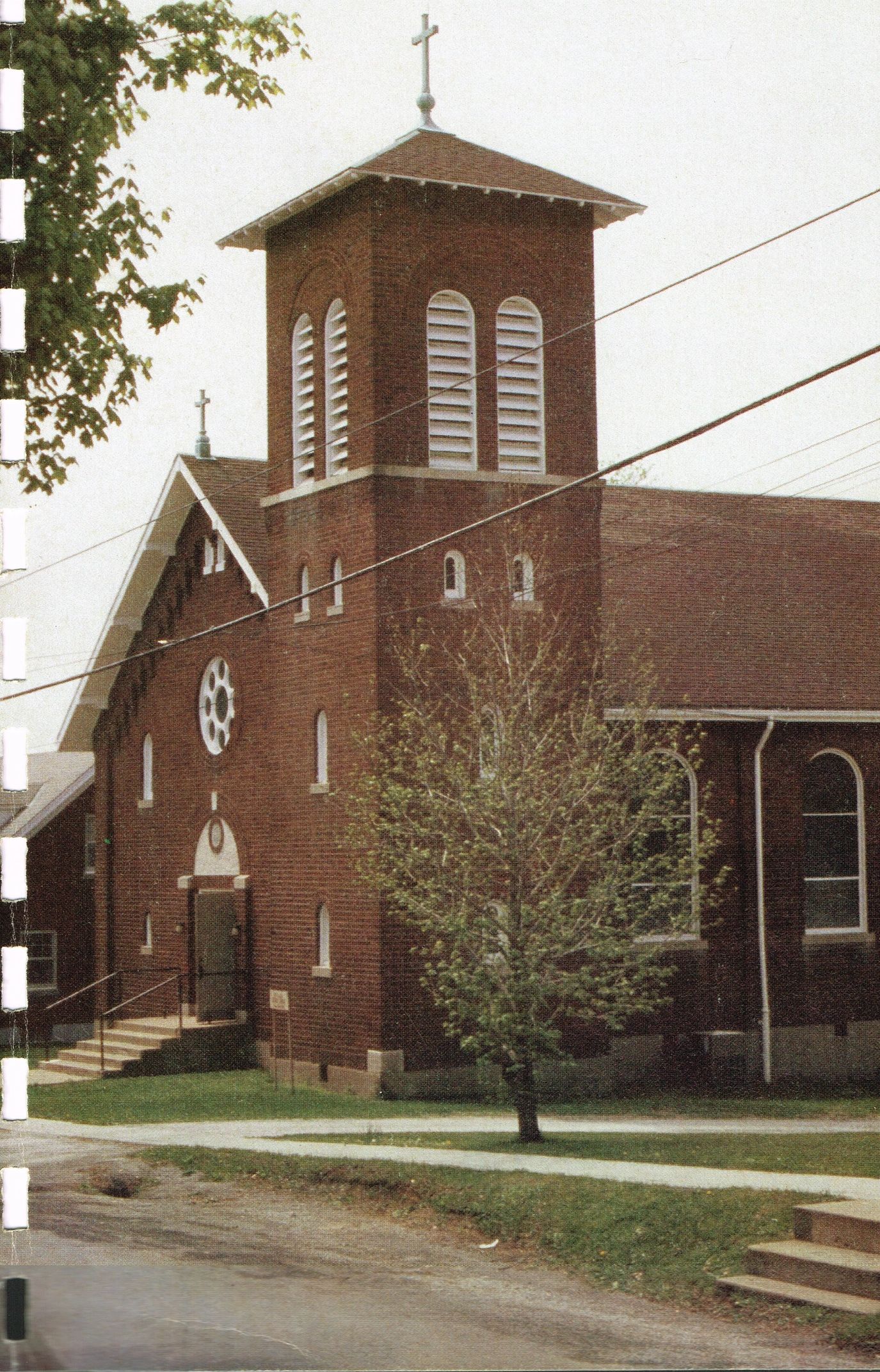 A brick church with a tall steeple and two crosses.