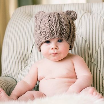 Baby wearing a knit bear hat sitting in a cozy chair during a Minneapolis newborn photo session.
