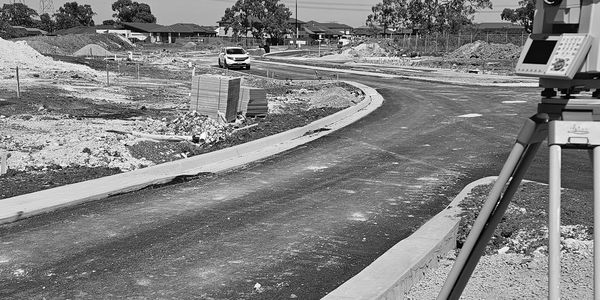Surveying equipment at a road construction site with a car and building materials.