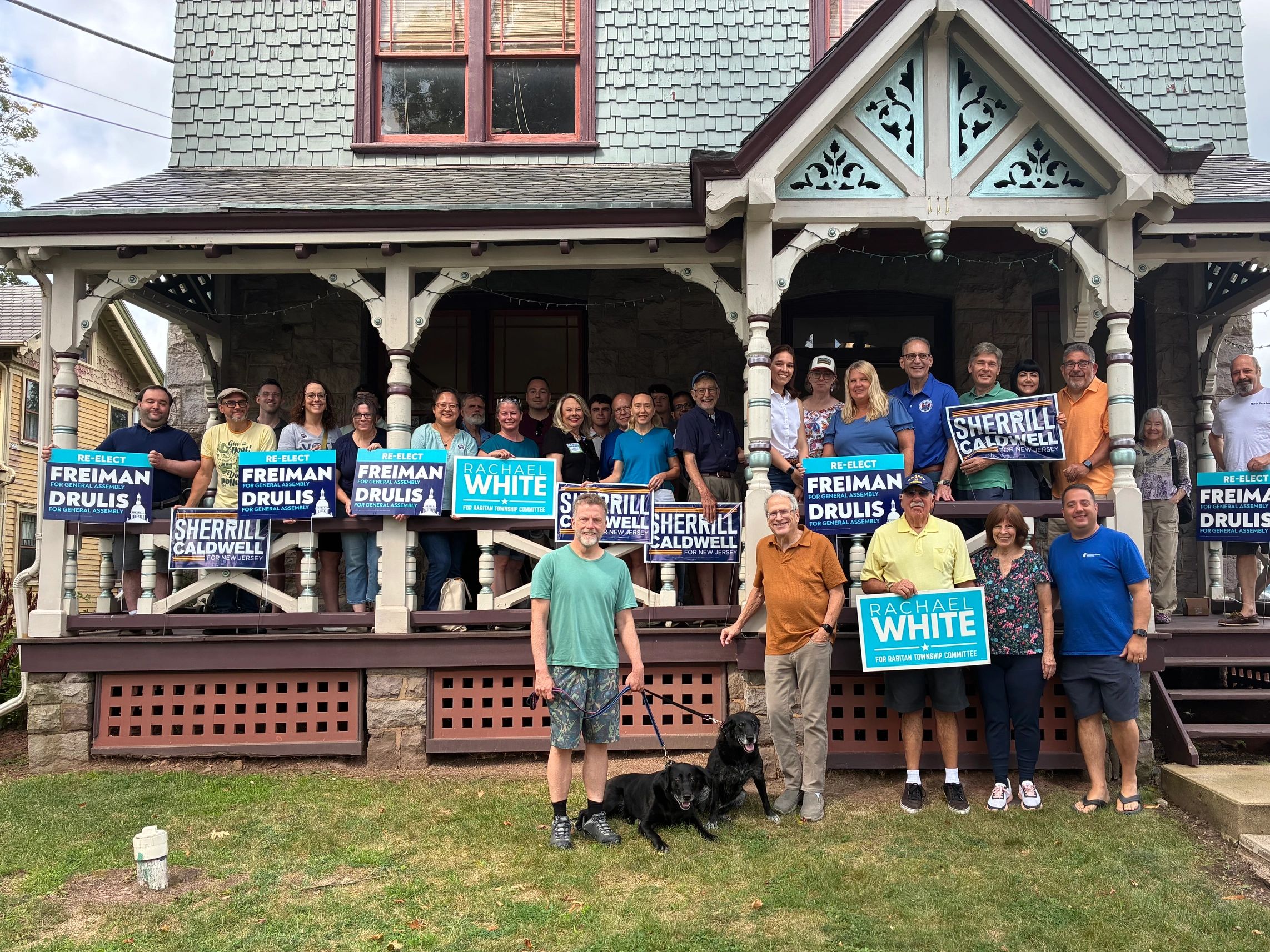 Group of people holding campaign signs on a porch of a house.